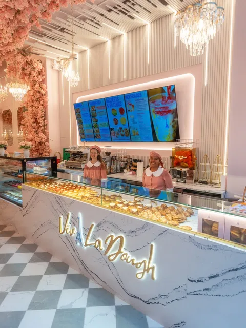 Midtown counter under a cherry-blossom arch, the pastry case lit beneath the Viva La Dough sign